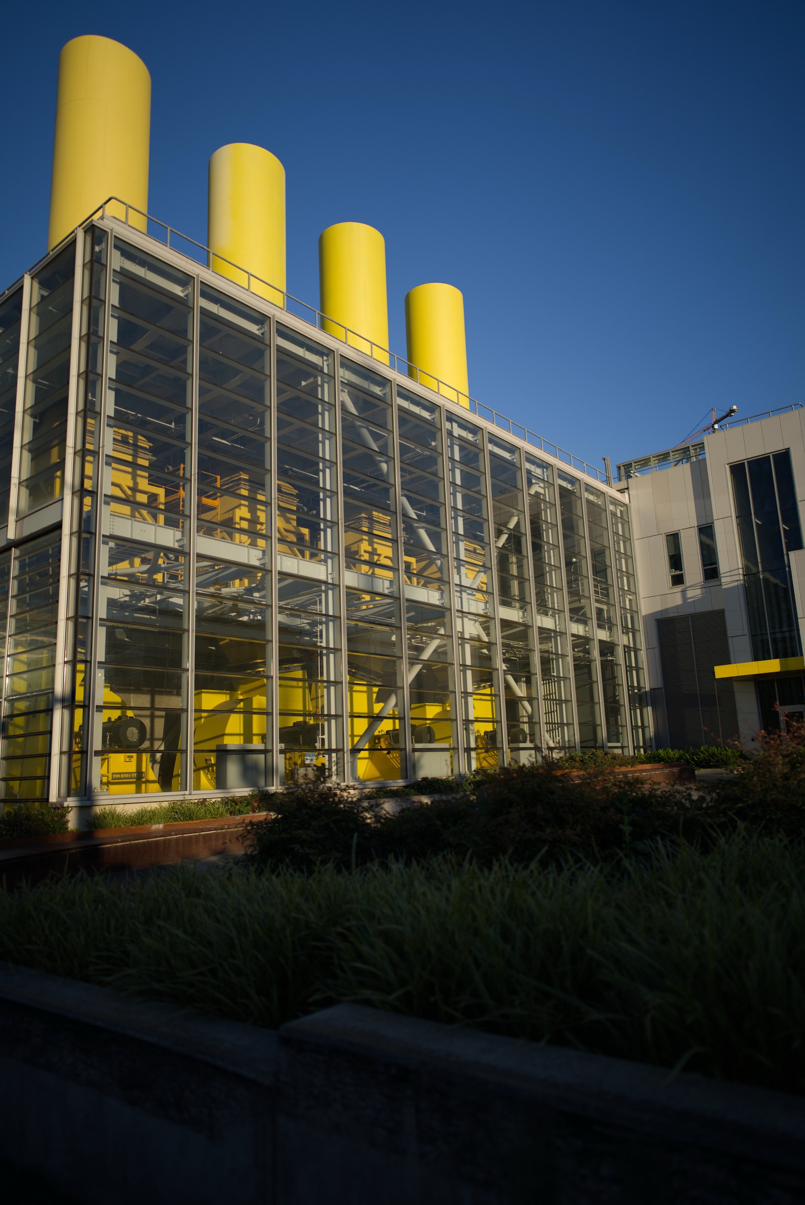 A glass-fronted building at golden hour with saturated yellow machinery visible inside.
