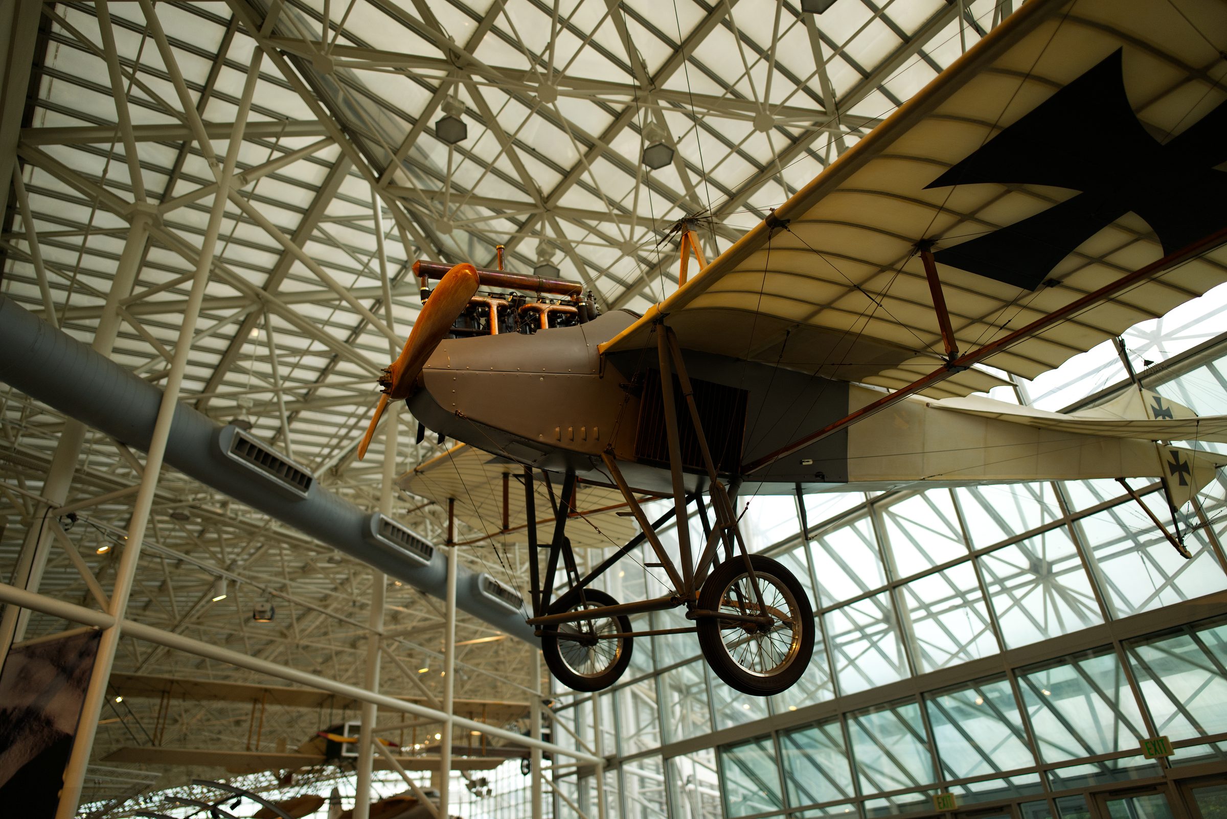 A hand-built early monoplane with exposed rigging, hanging under a glass museum roof.